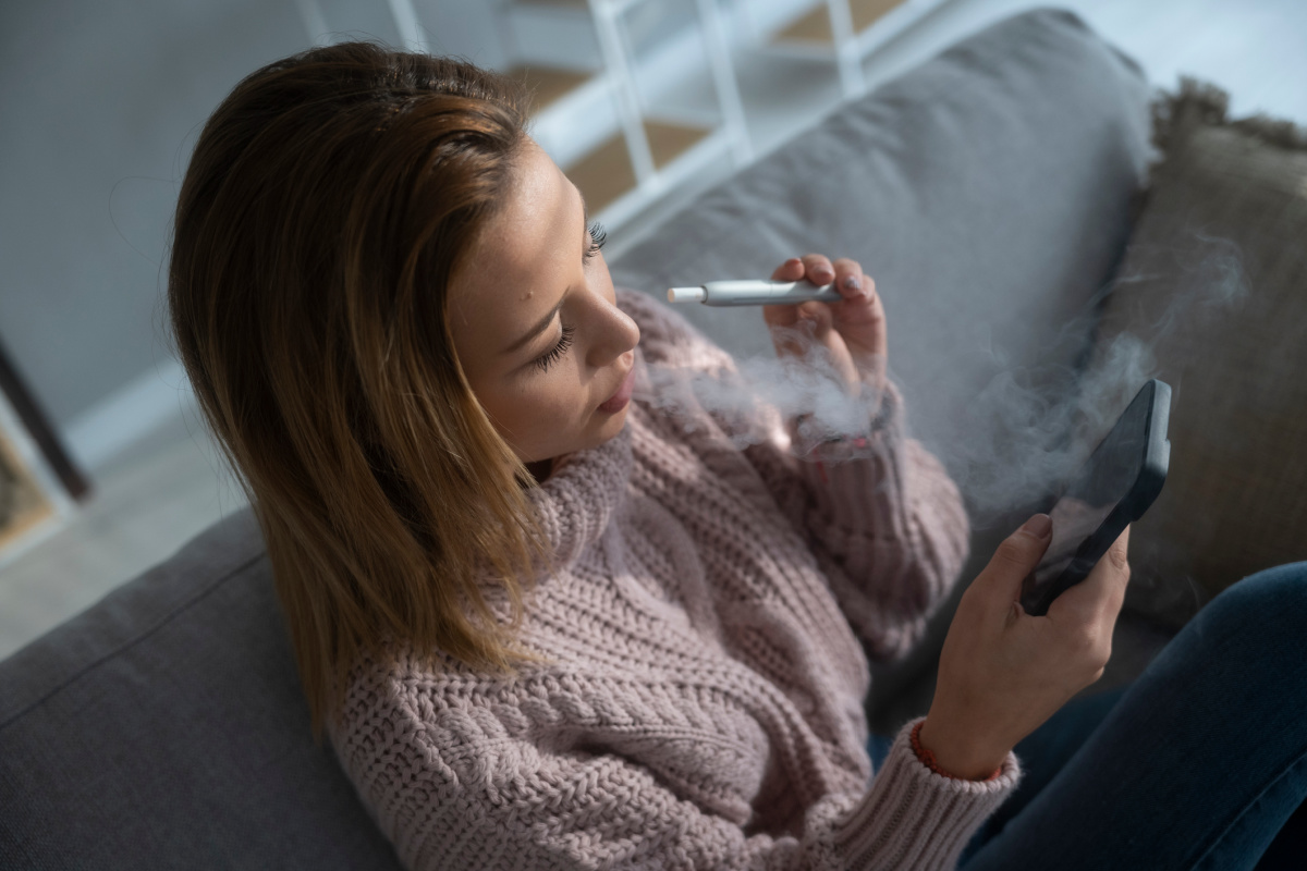 Woman relaxing on the couch with her phone while vaping an e-cig