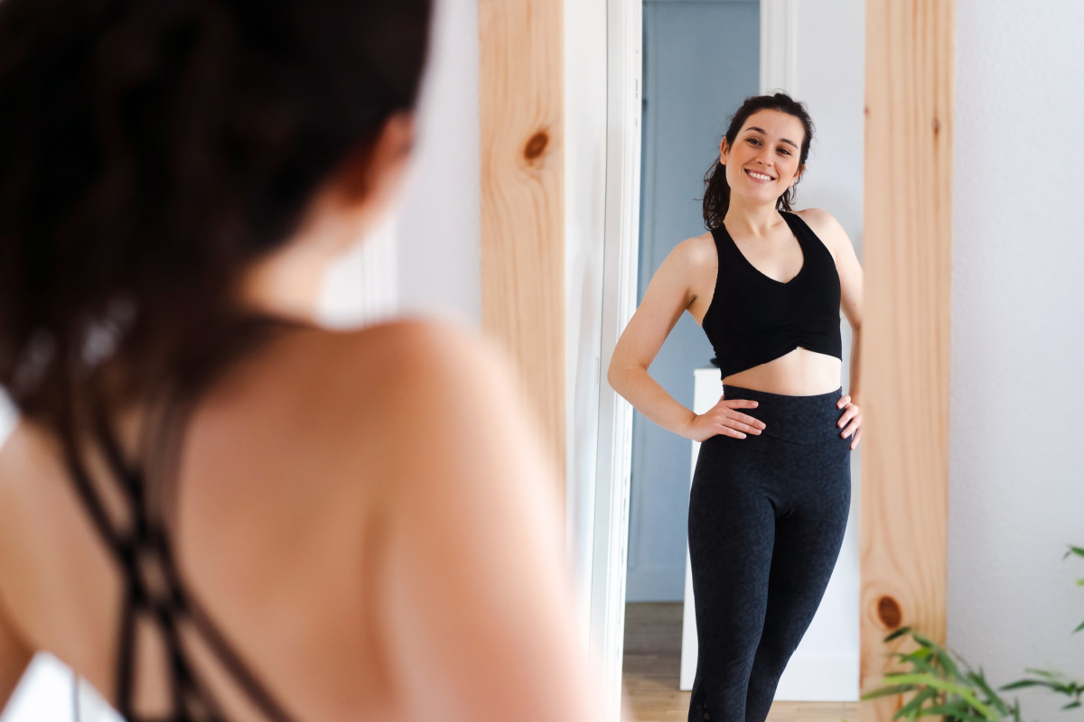 Young happy woman looking in the mirror satisfied with the results of post weight loss body lift procedure