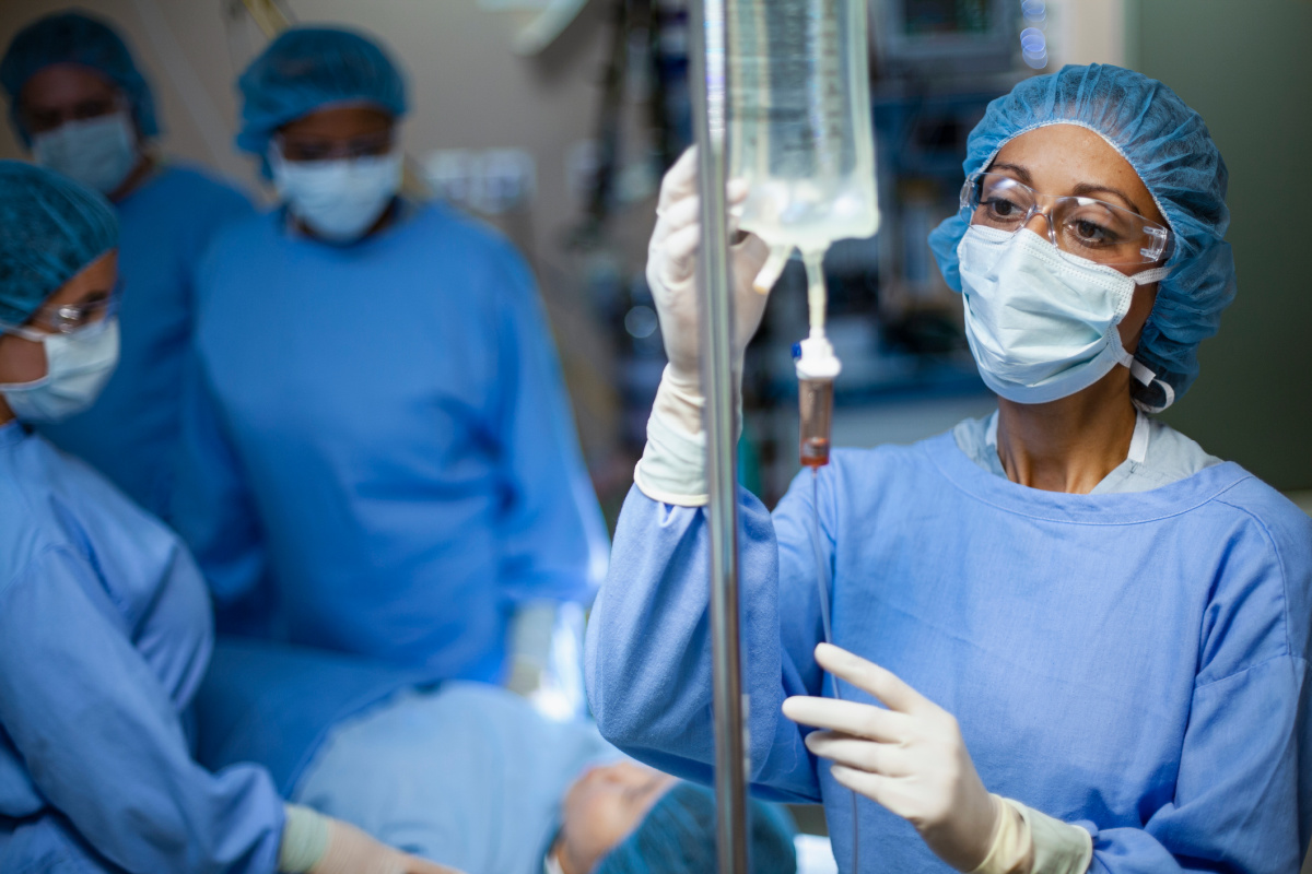 A board-certified anesthesiologist monitoring a patient's IV drip during a plastic surgery procedure